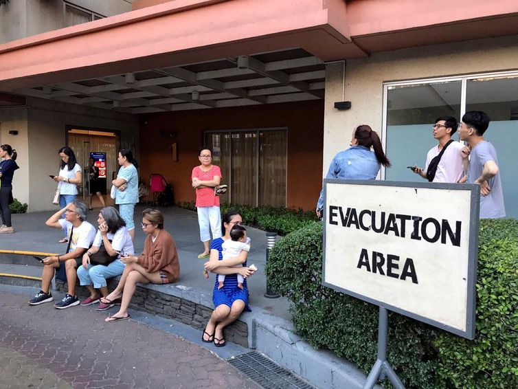 Moradores se sentam do lado de fora depois de serem evacuados do prédio do condomínio após um terremoto na cidade de Makati